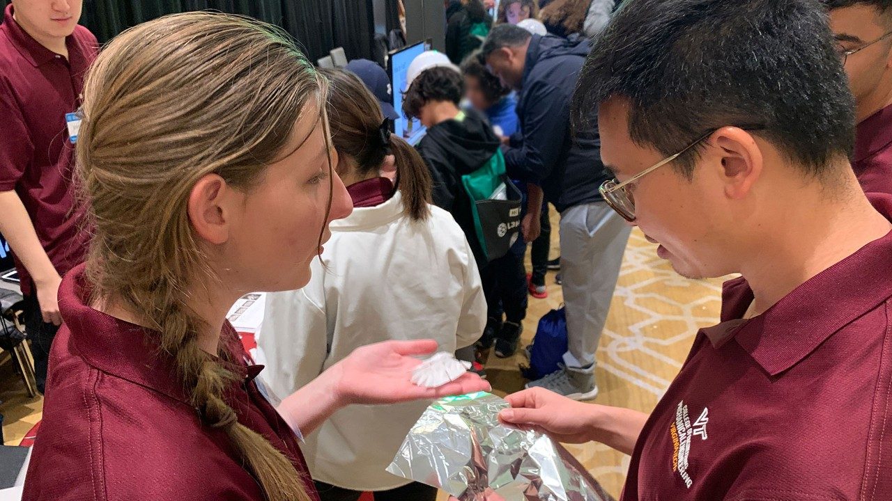 Savannah Peters talks with Suyi Li about an origami fold for a nearby booth at the Sea-Air-Space STEM expo. Photo by Alex Parrish for Virginia Tech.