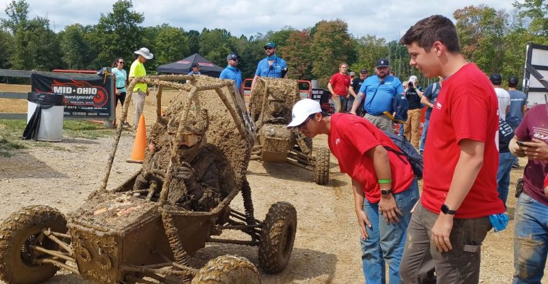 (Left to right) Driver Steven Little returns from a muddy test run to touch base with Baja members Baile Liu and Peter Mercatili. Photo courtesy of VT Baja.