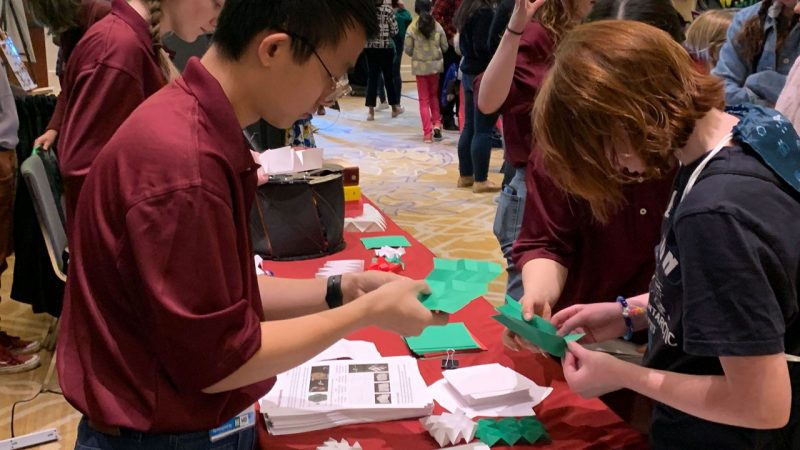 Roy Luo works with a student to finish an origami fold at the Sea-Air-Space STEM expo. Photo by Alex Parrish for Virginia Tech.